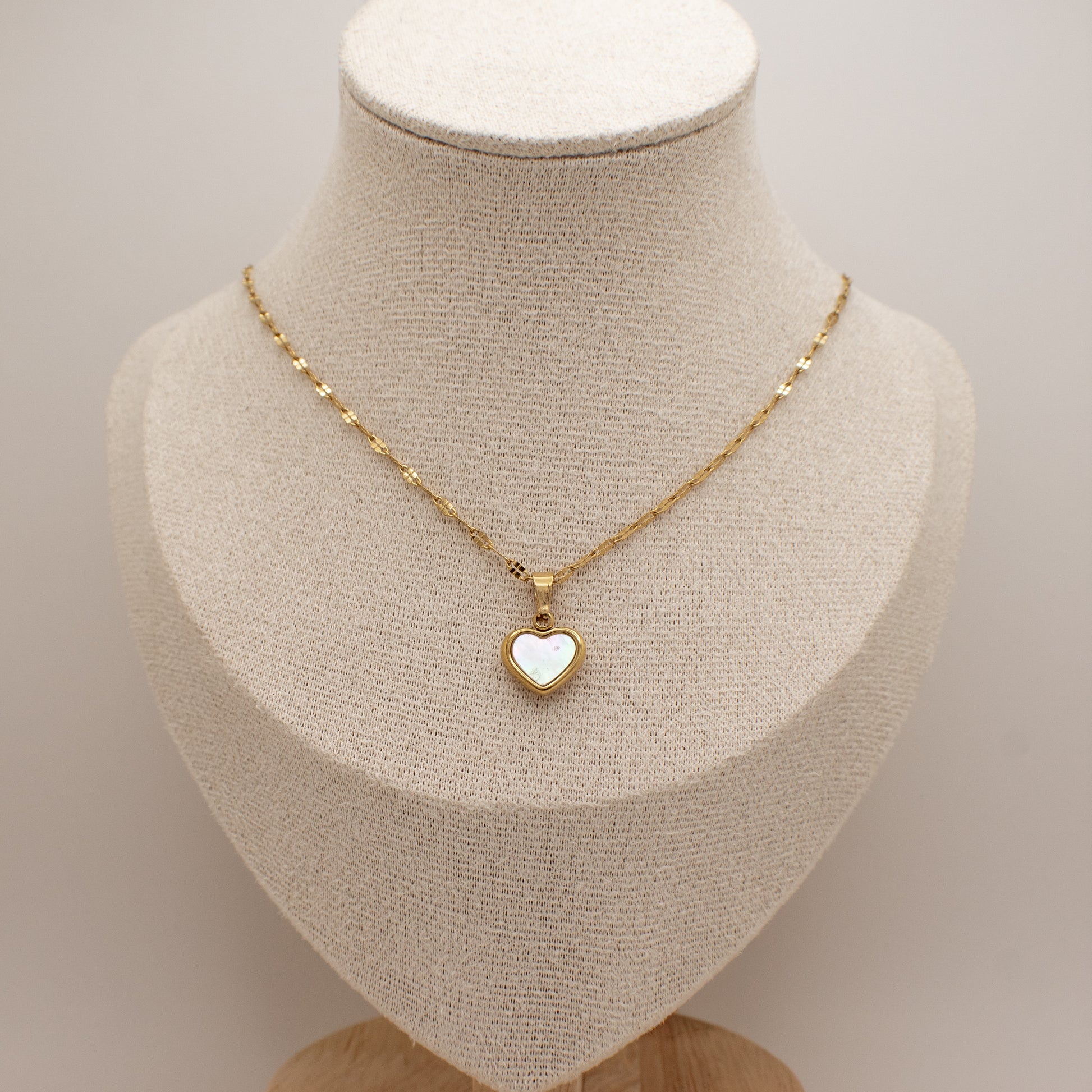 Gold necklace with a heart-shaped pendant on a mannequin bust.