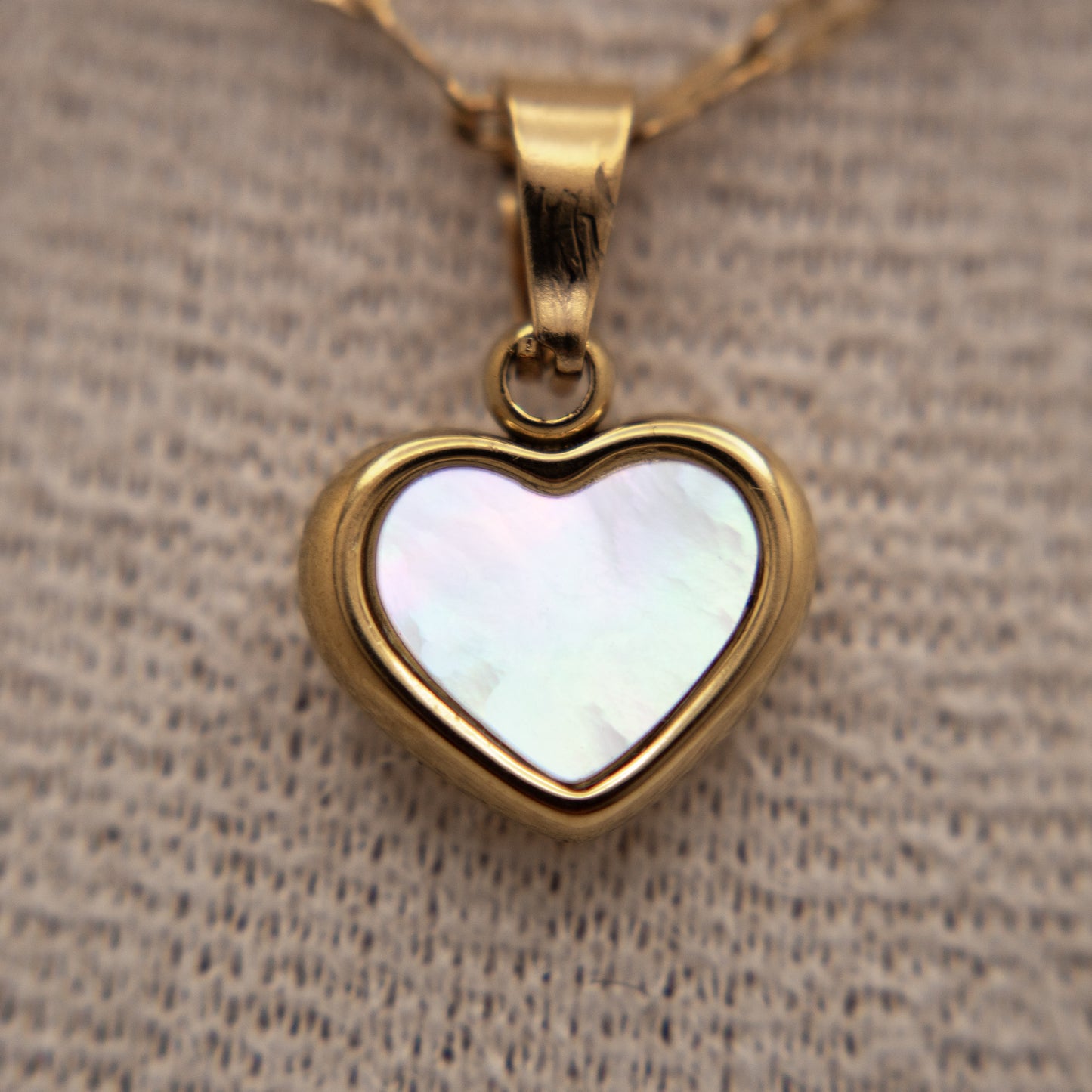 Heart-shaped pendant with a white center on a textured beige background