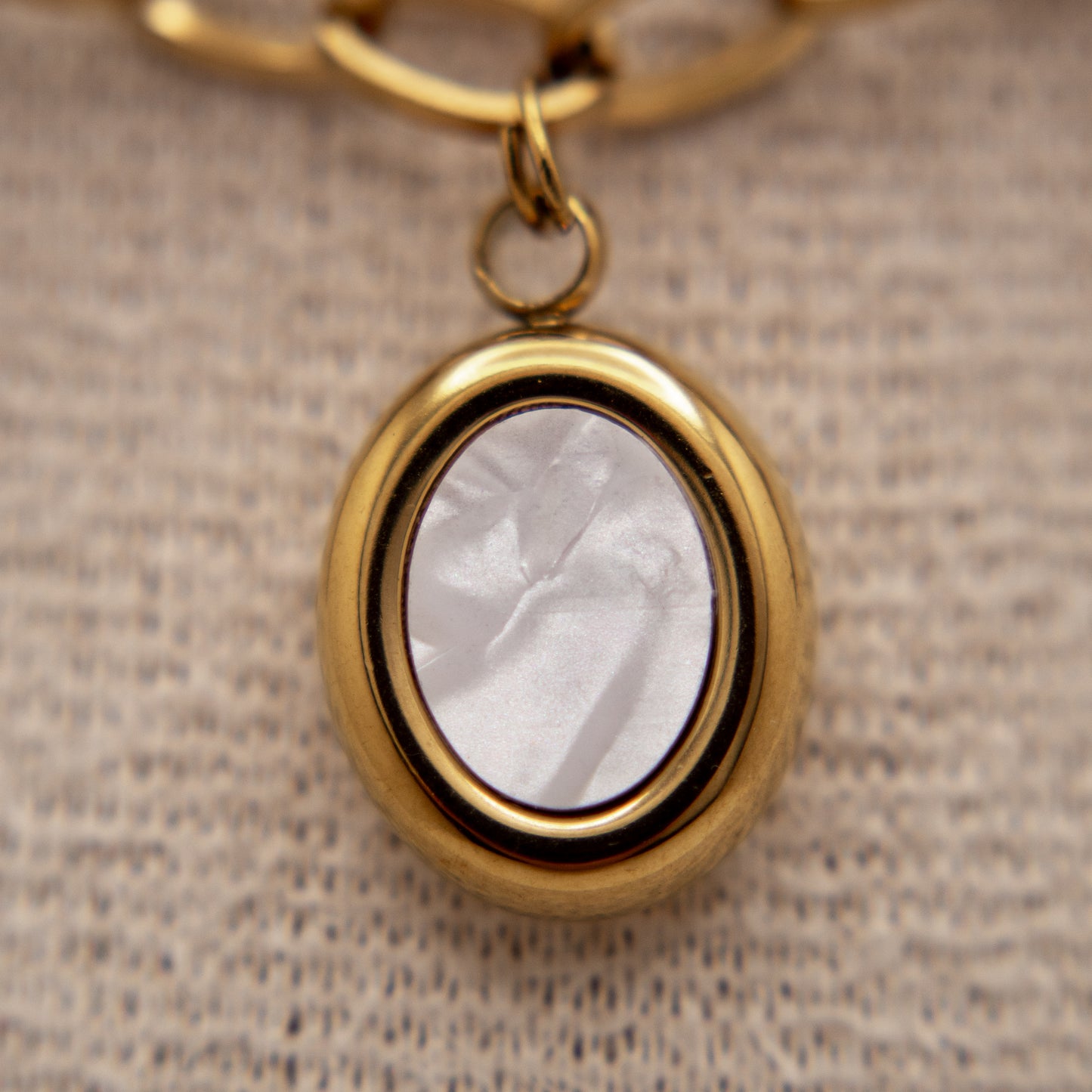Gold pendant with a white stone on a textured beige background