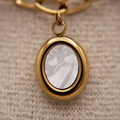 Gold pendant with a white stone on a textured beige background