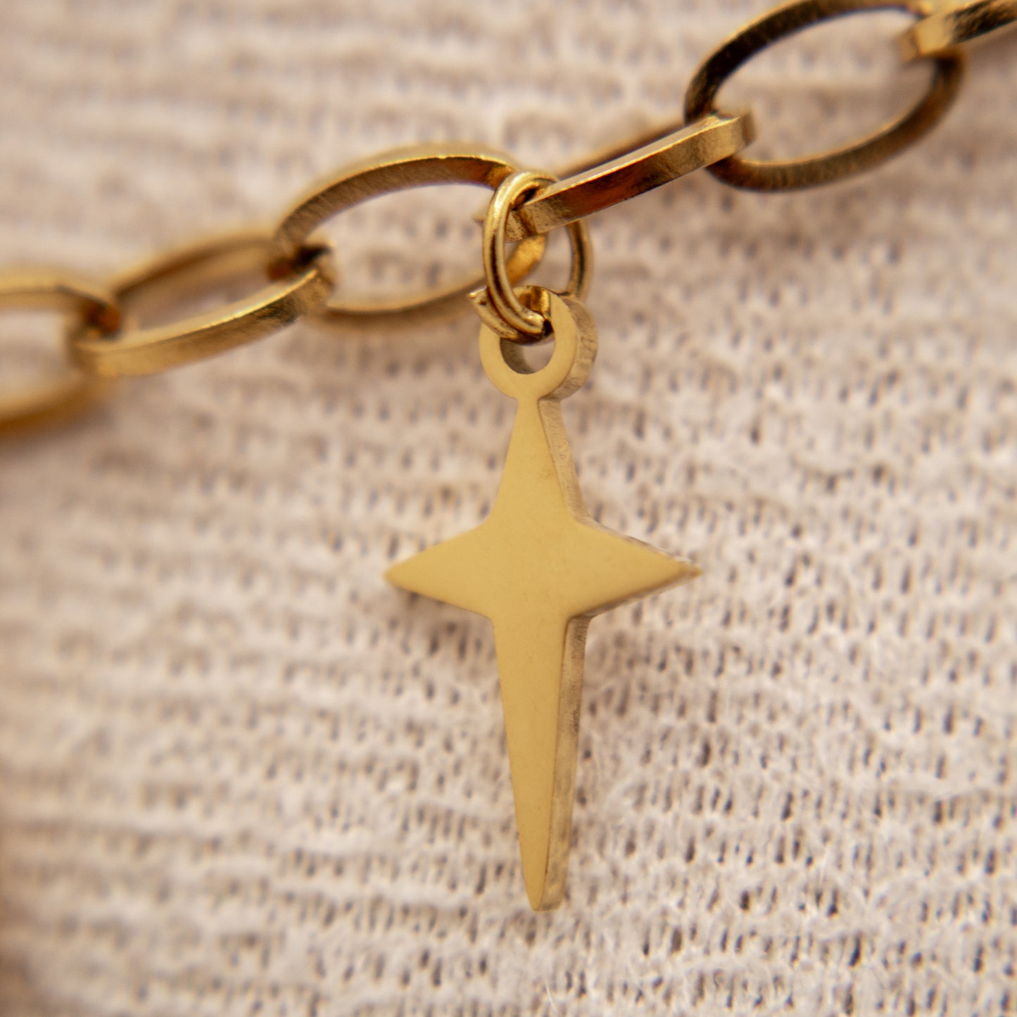 Gold chain bracelet with a star-shaped pendant on a beige textured background
