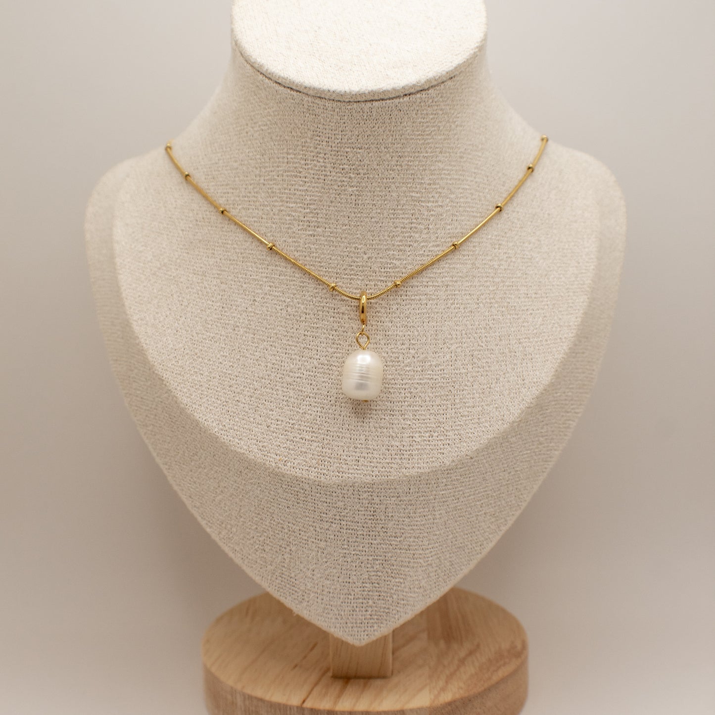 Gold necklace with a pearl pendant on a mannequin bust against a neutral background