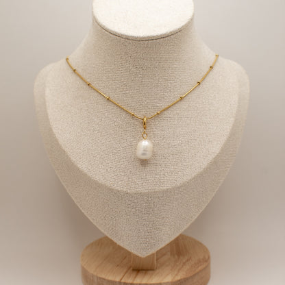 Gold necklace with a pearl pendant on a mannequin bust against a neutral background
