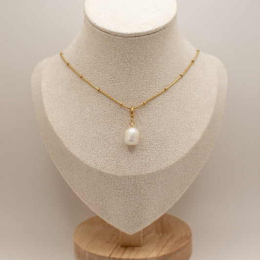 Gold necklace with a pearl pendant on a mannequin bust against a neutral background