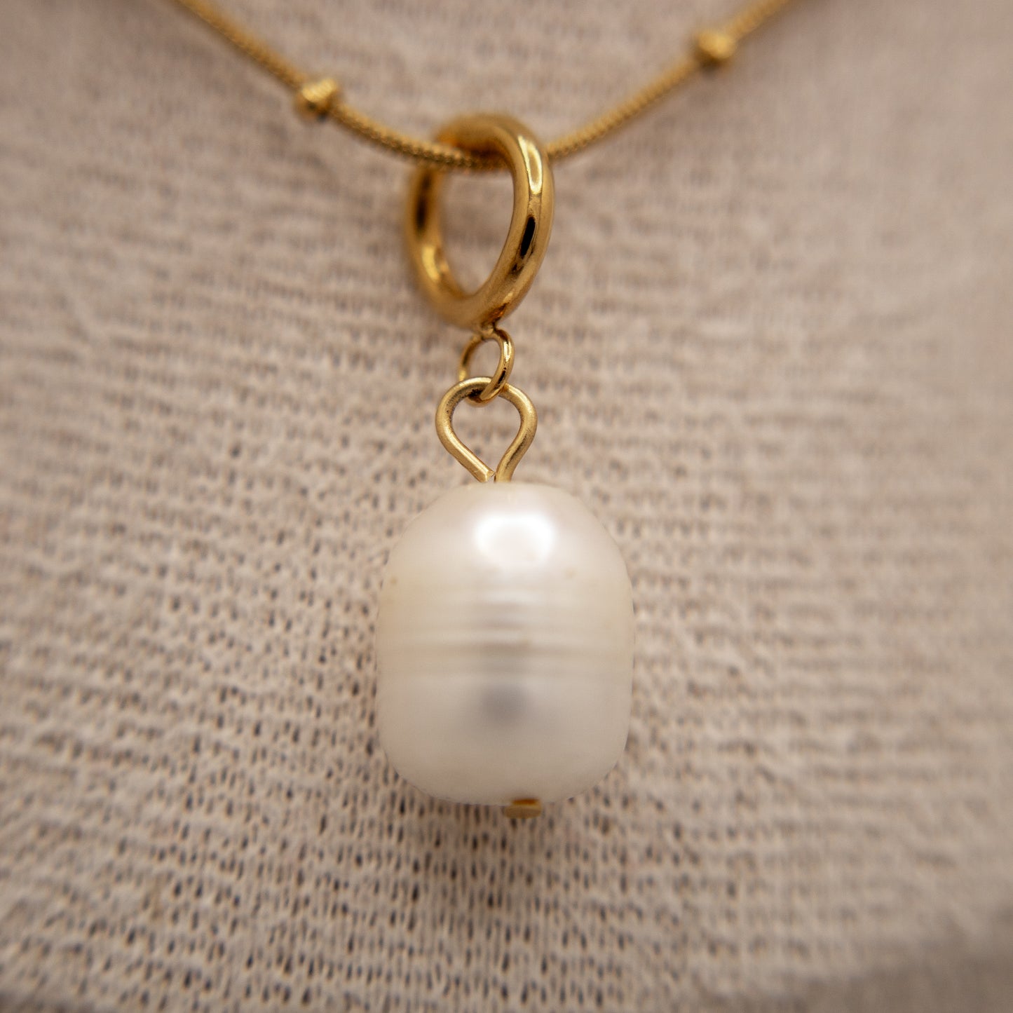 Gold necklace with a pearl pendant on a textured beige background