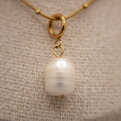 Gold necklace with a pearl pendant on a textured beige background