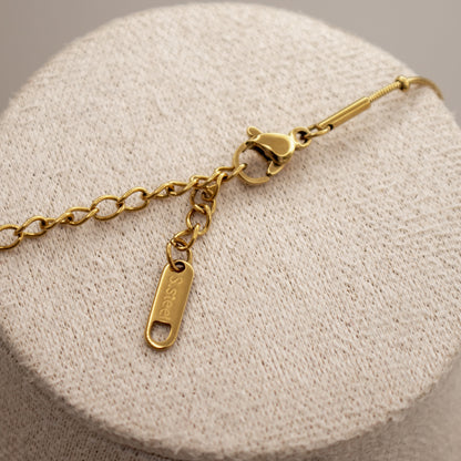 Gold bracelet with a tag on a beige cushion