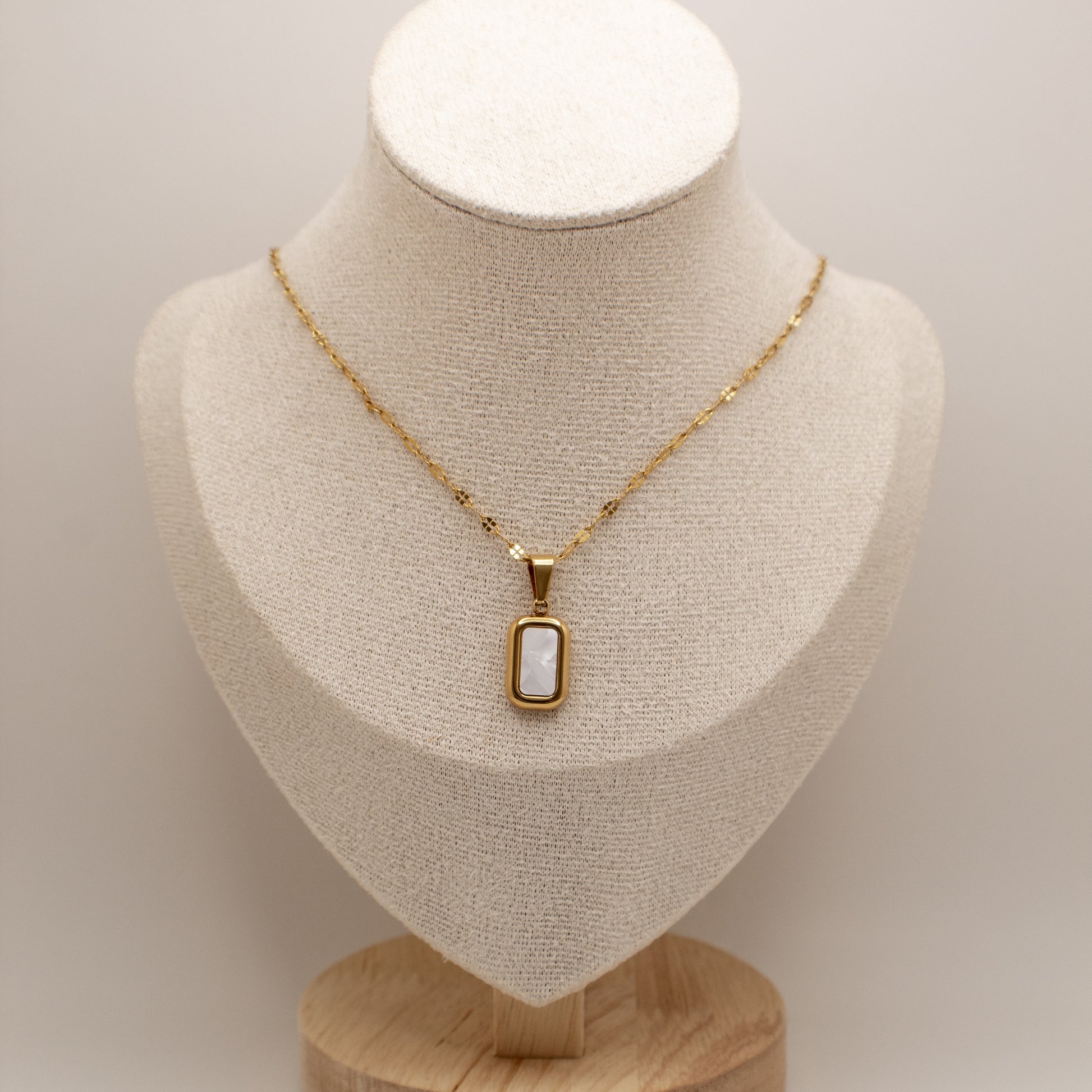 Gold necklace with a pendant on a mannequin bust against a neutral background