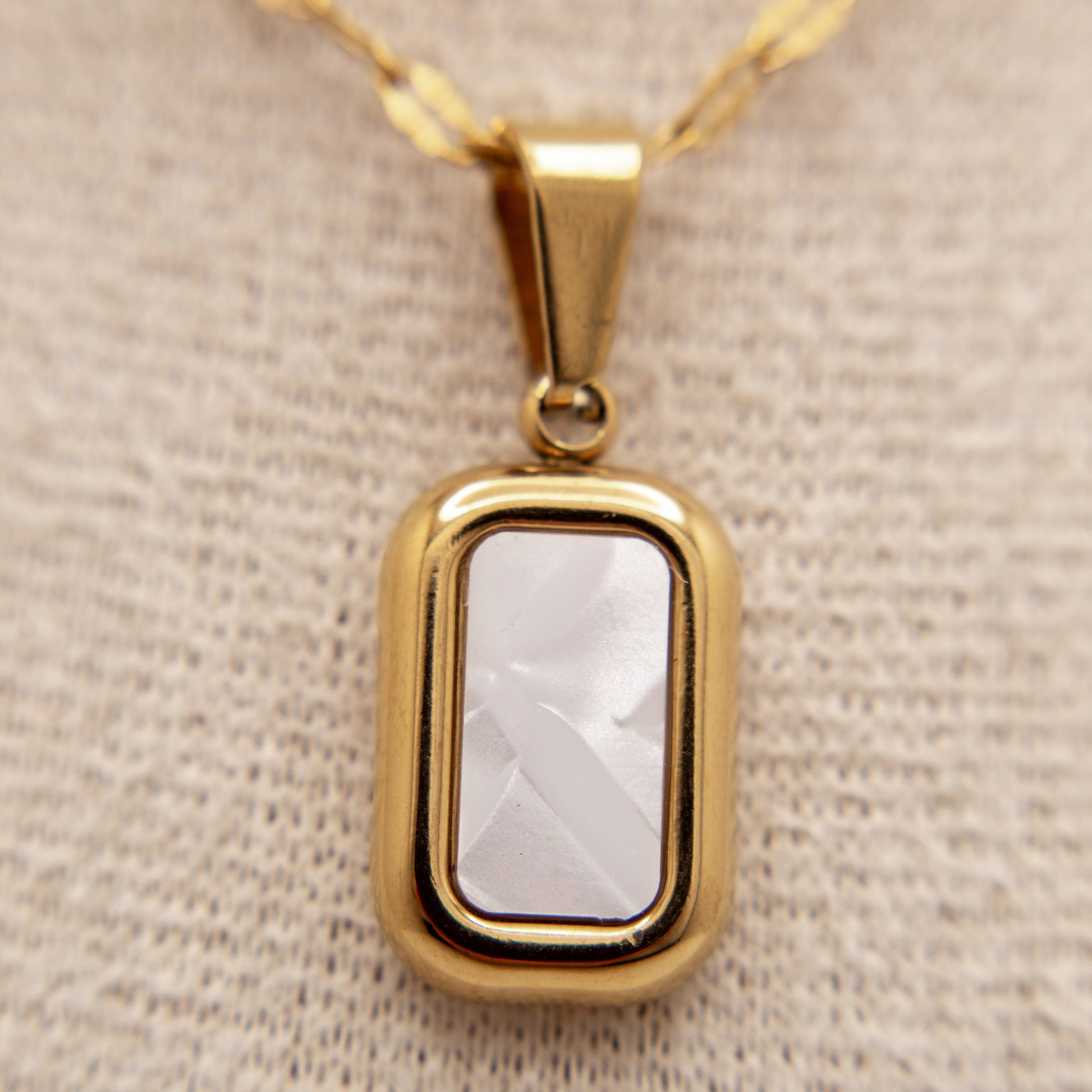 Gold pendant with a clear stone on a beige fabric background