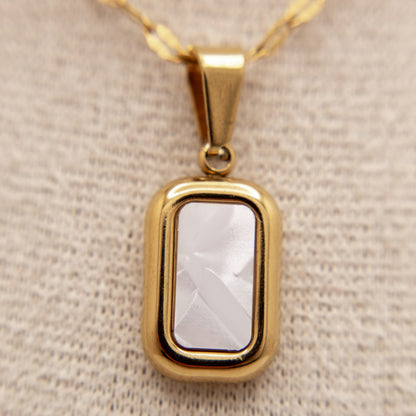 Gold pendant with a clear stone on a beige fabric background
