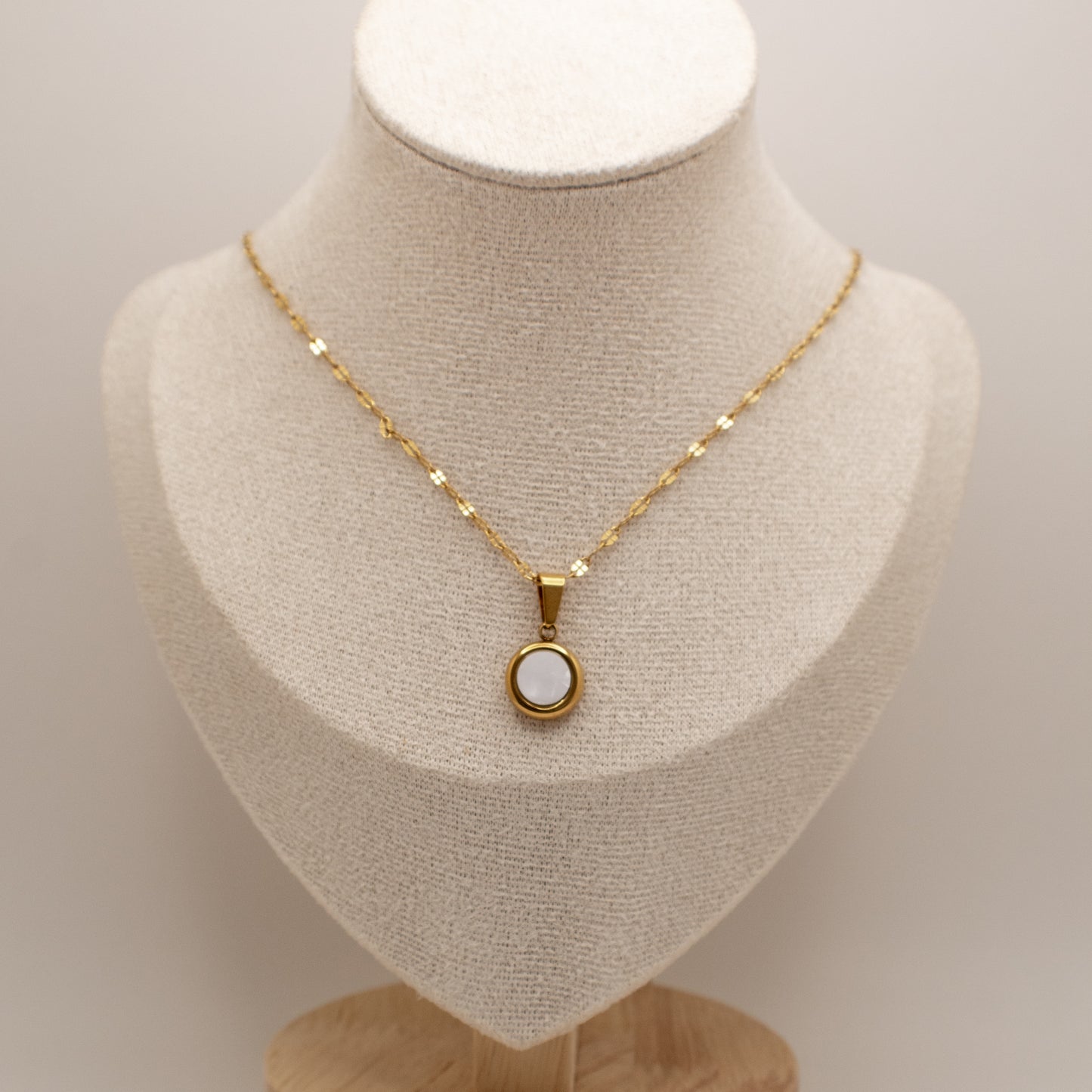 Gold necklace with a pendant on a mannequin bust against a neutral background