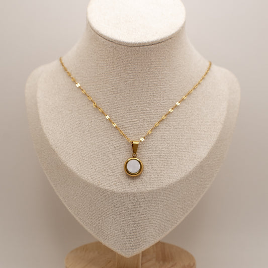 Gold necklace with a pendant on a mannequin bust against a neutral background