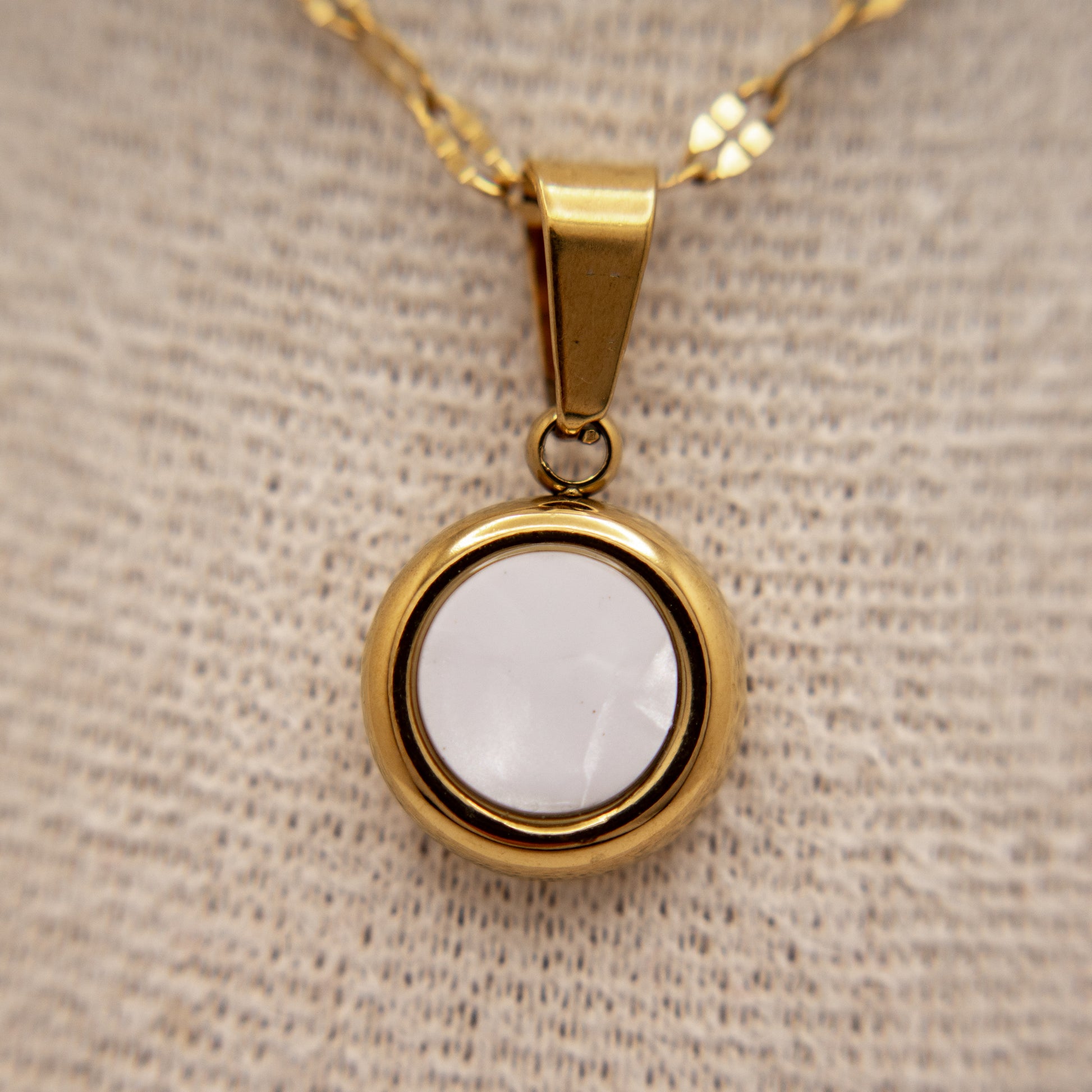 Gold pendant with a white stone on a beige fabric background