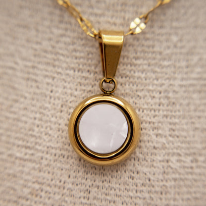 Gold pendant with a white stone on a beige fabric background