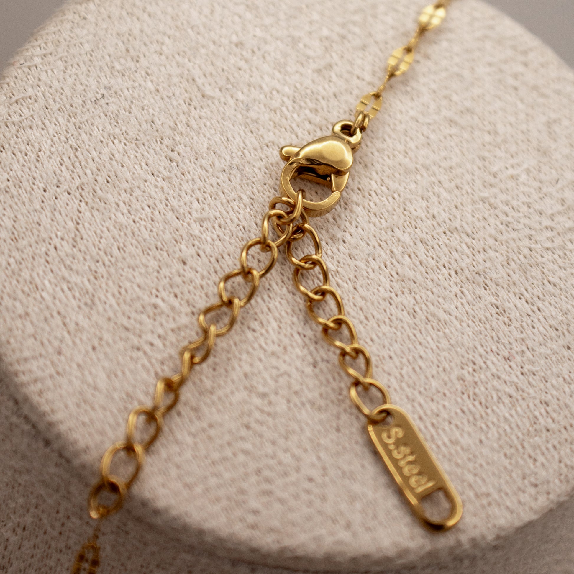 Gold bracelet with a clasp and tag on a textured beige surface