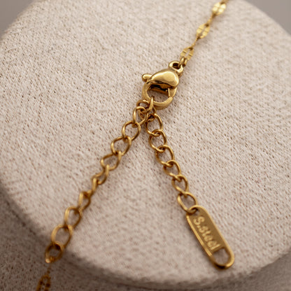 Gold bracelet with a clasp and tag on a textured beige surface
