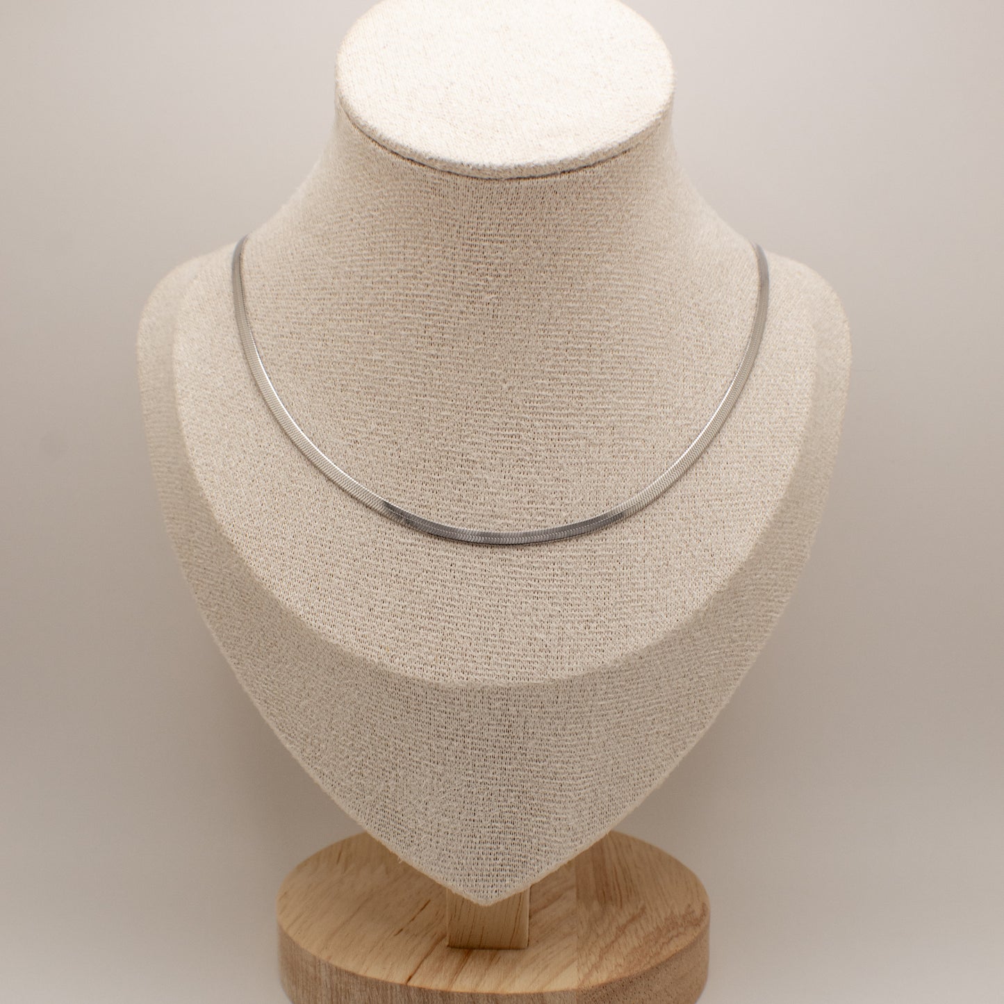Silver necklace on a beige mannequin bust with a wooden base against a light background