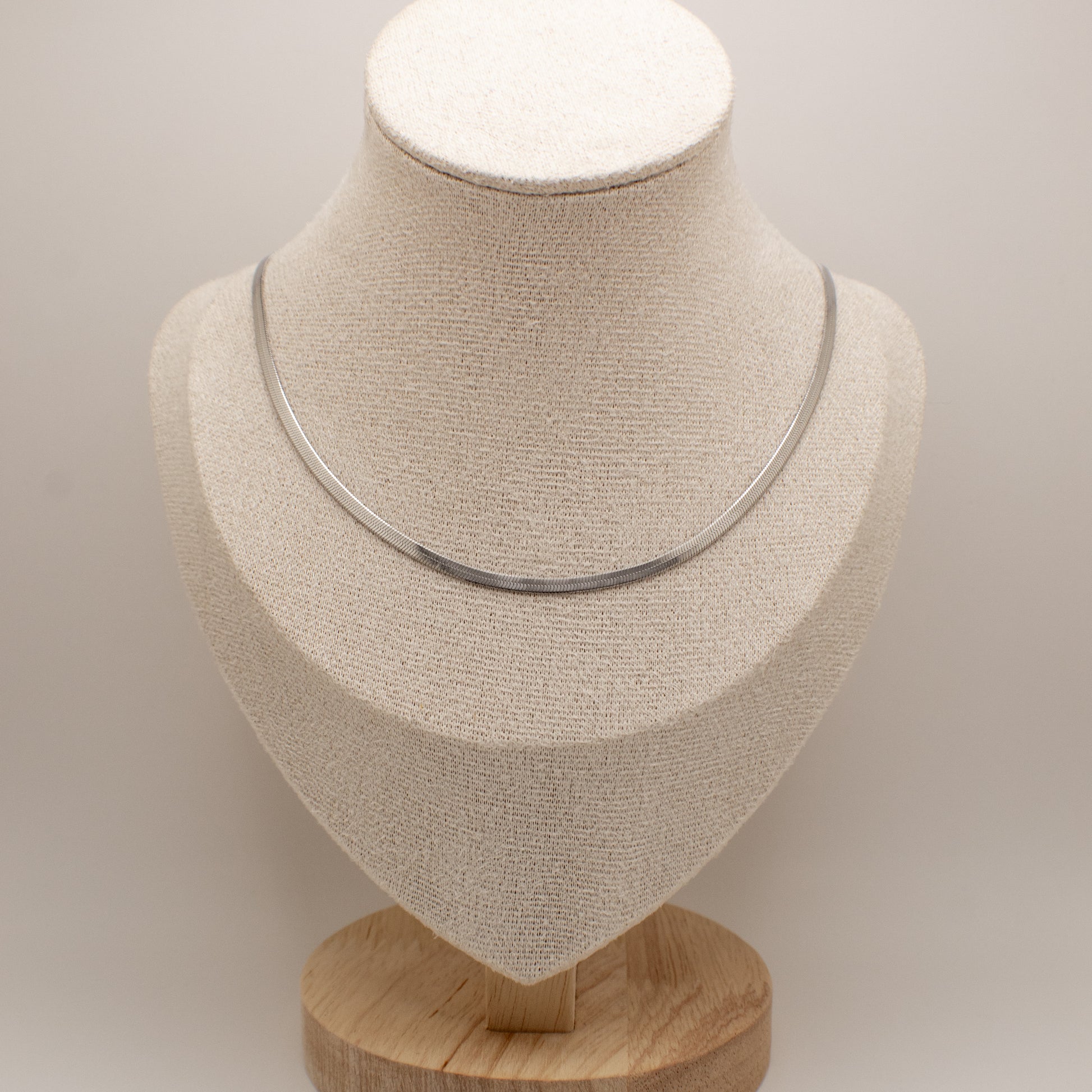 Silver necklace on a beige mannequin bust with a wooden base against a light background