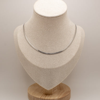 Silver necklace on a beige mannequin bust with a wooden base against a light background