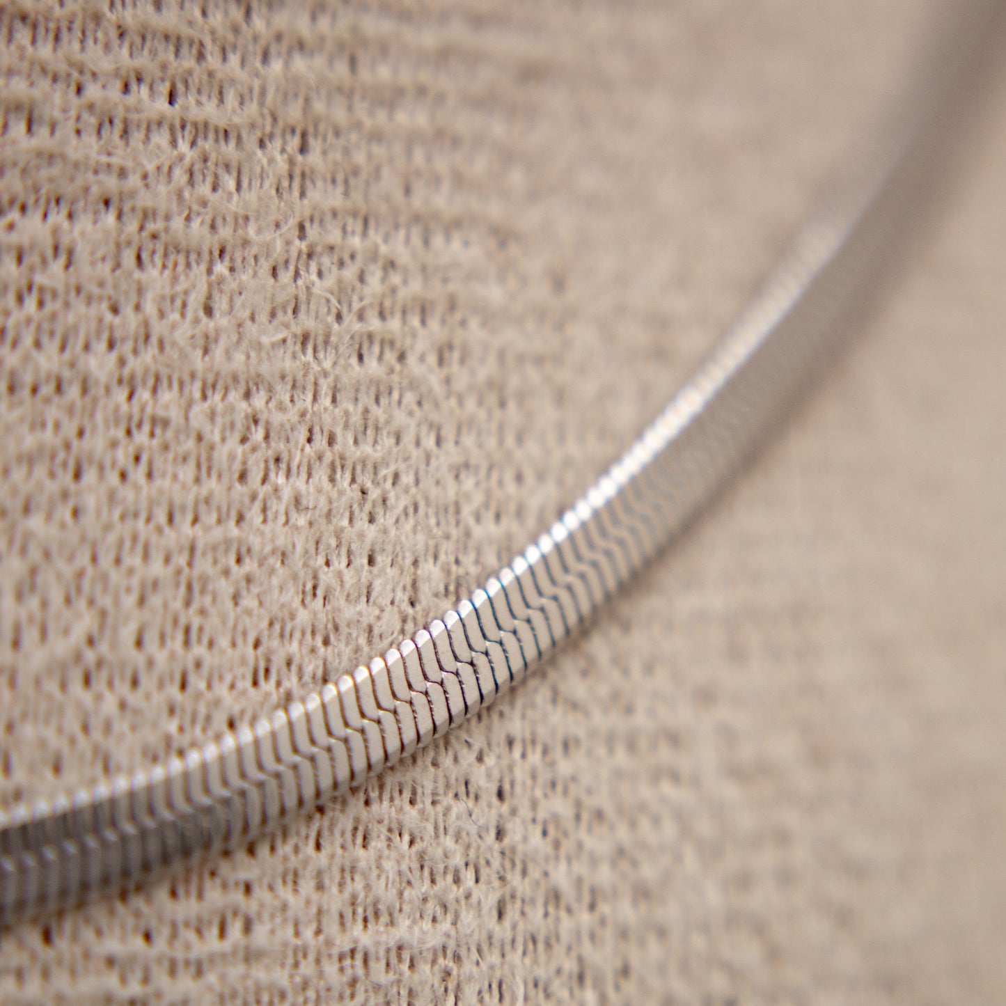 Close-up of a textured silver necklace on a beige fabric background