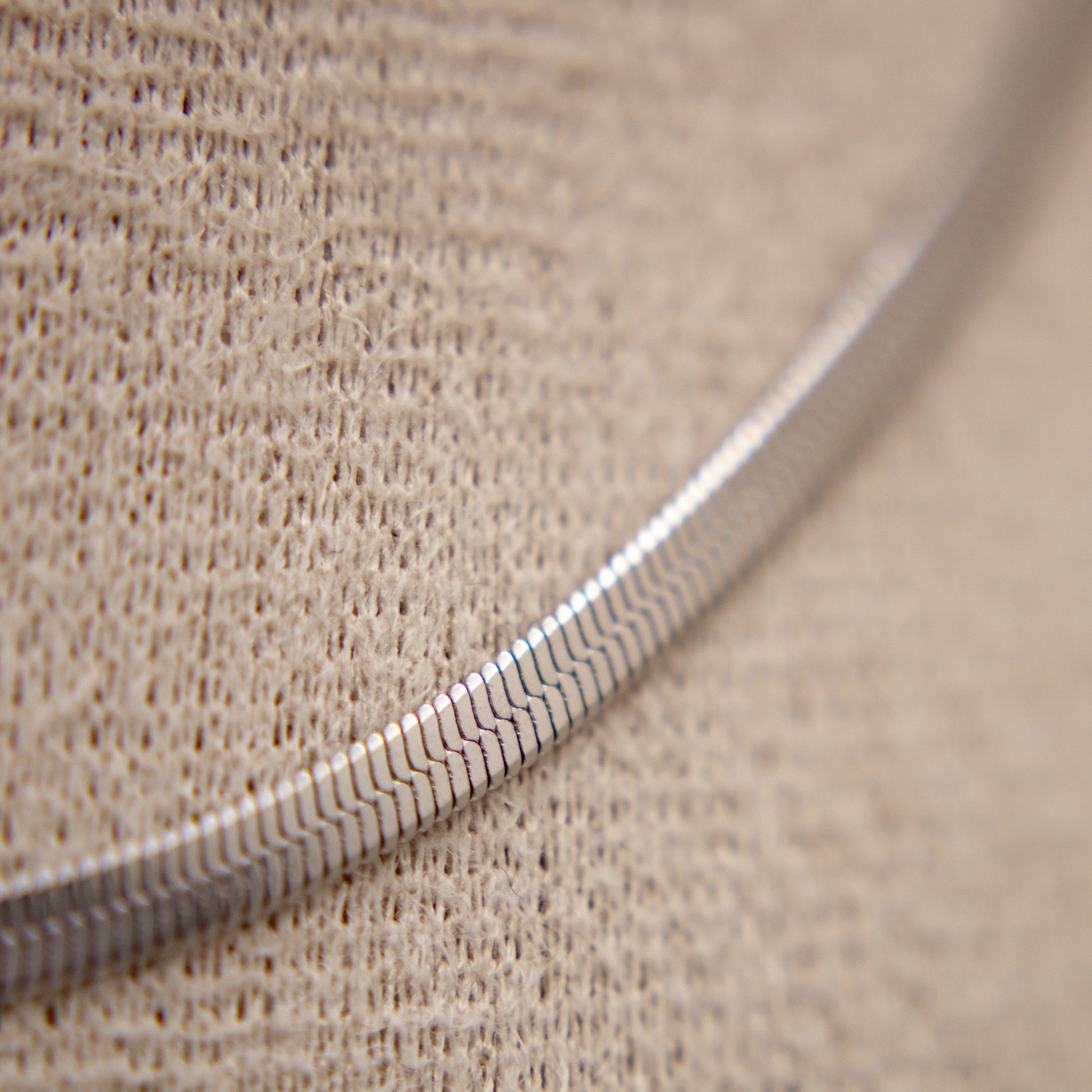 Close-up of a textured silver necklace on a beige fabric background