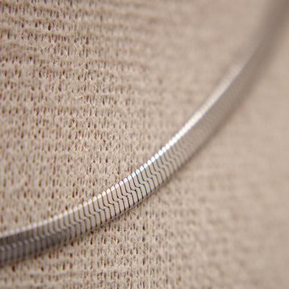 Close-up of a textured silver necklace on a beige fabric background