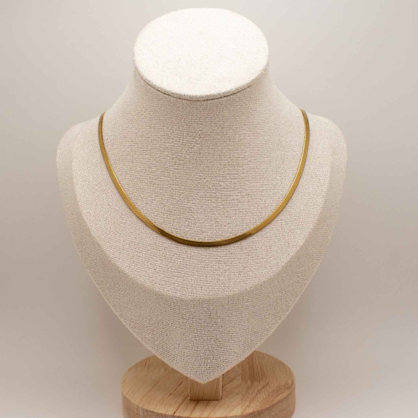 Gold necklace on a beige bust with a wooden base against a light gray background