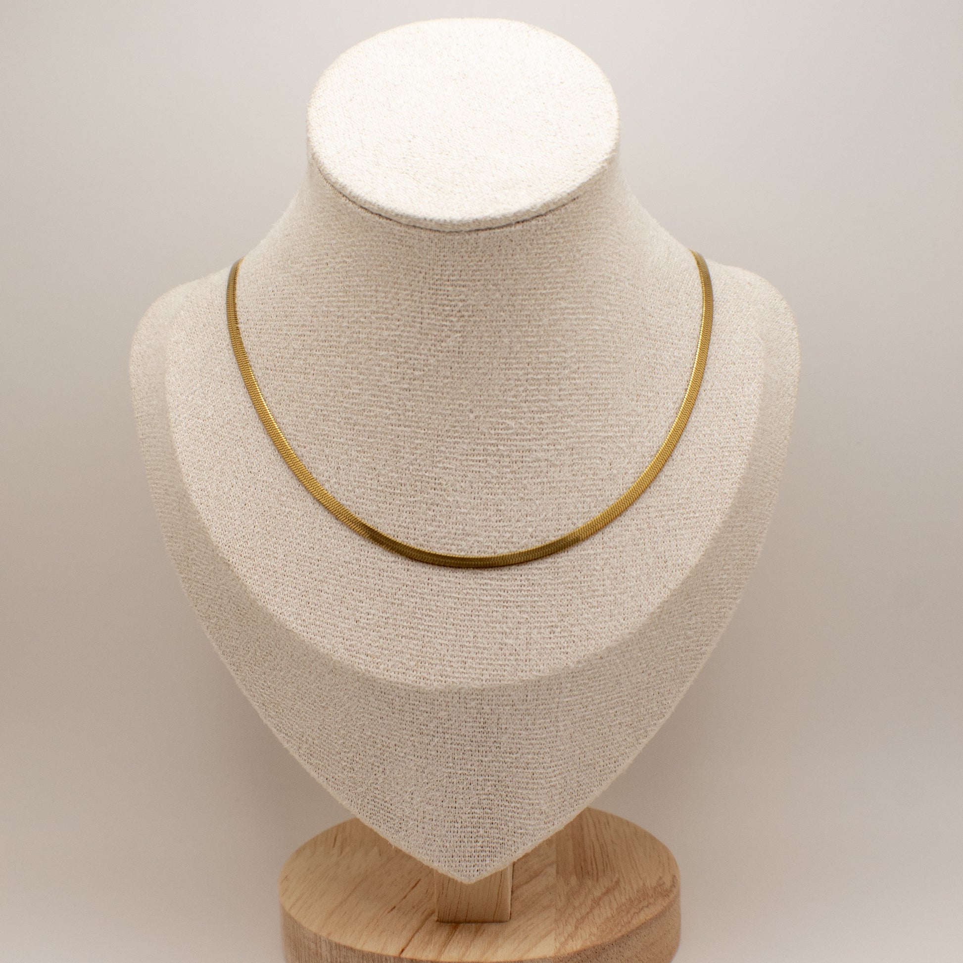 Gold necklace on a beige bust with a wooden base against a light gray background
