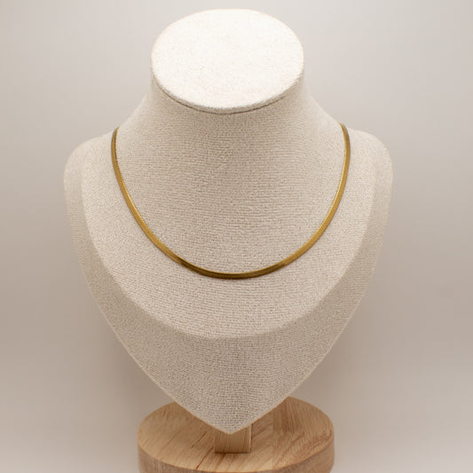 Gold necklace on a beige bust with a wooden base against a light gray background