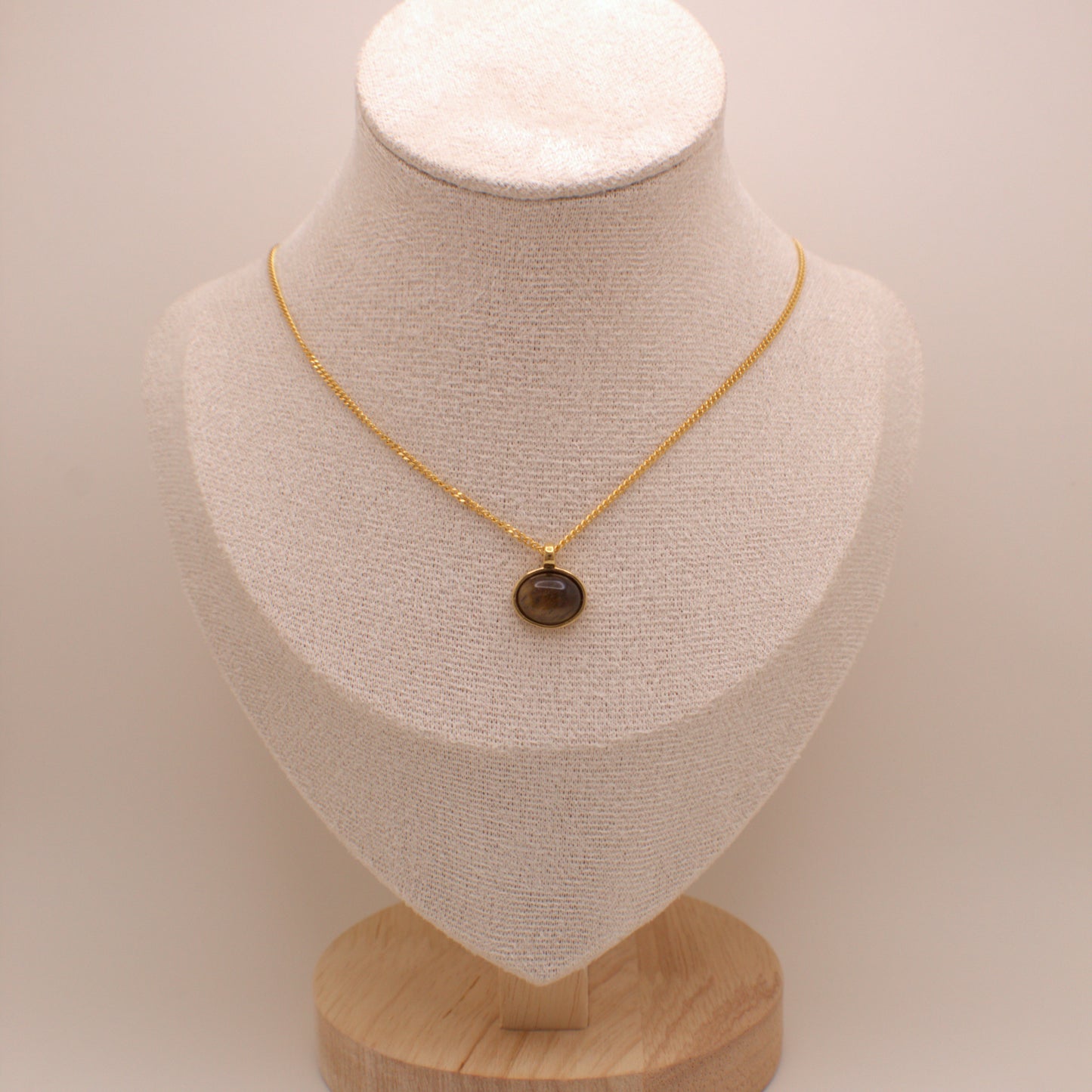 Gold necklace with a brown pendant on a beige mannequin bust against a beige background