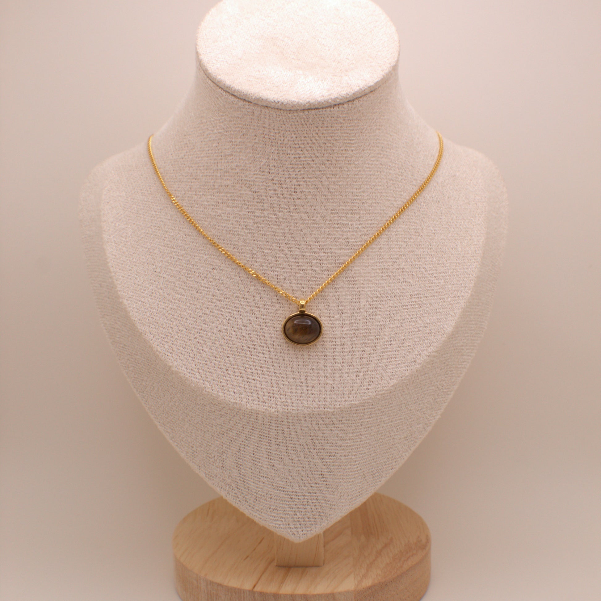 Gold necklace with a brown pendant on a beige mannequin bust against a beige background