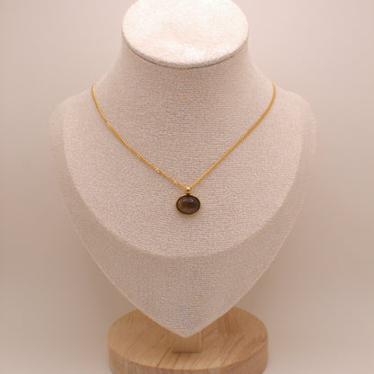 Gold necklace with a brown pendant on a beige mannequin bust against a beige background