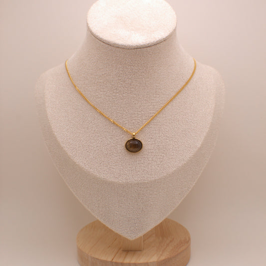 Gold necklace with a brown pendant on a beige mannequin bust against a beige background