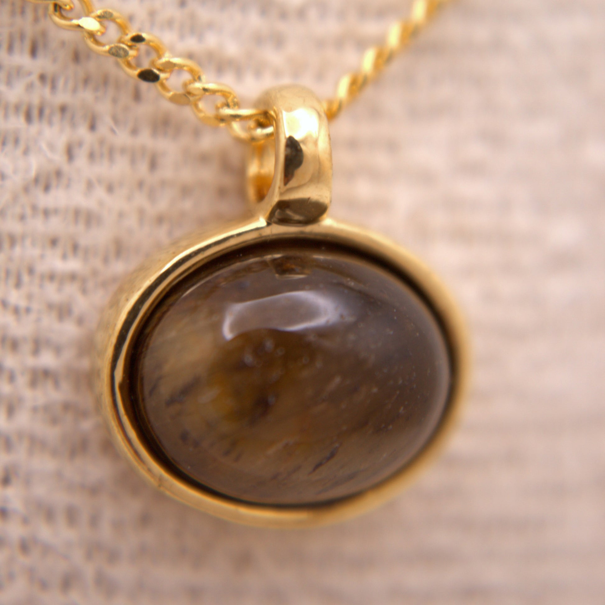Gold necklace with a dark stone pendant on a textured beige background