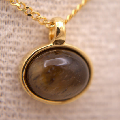 Gold necklace with a dark stone pendant on a textured beige background