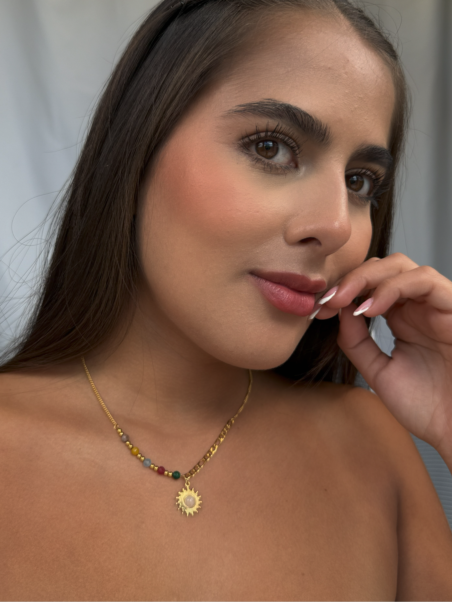 Gold necklace with small sun charm and white stone center, paired with colorful beads.