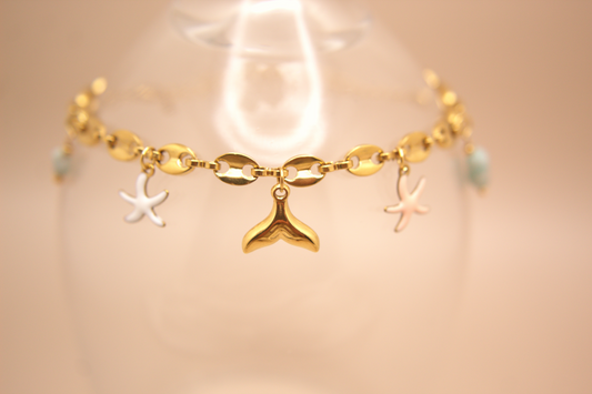 Golden bracelet featuring enamel starfish in white and pink with whale tail charm