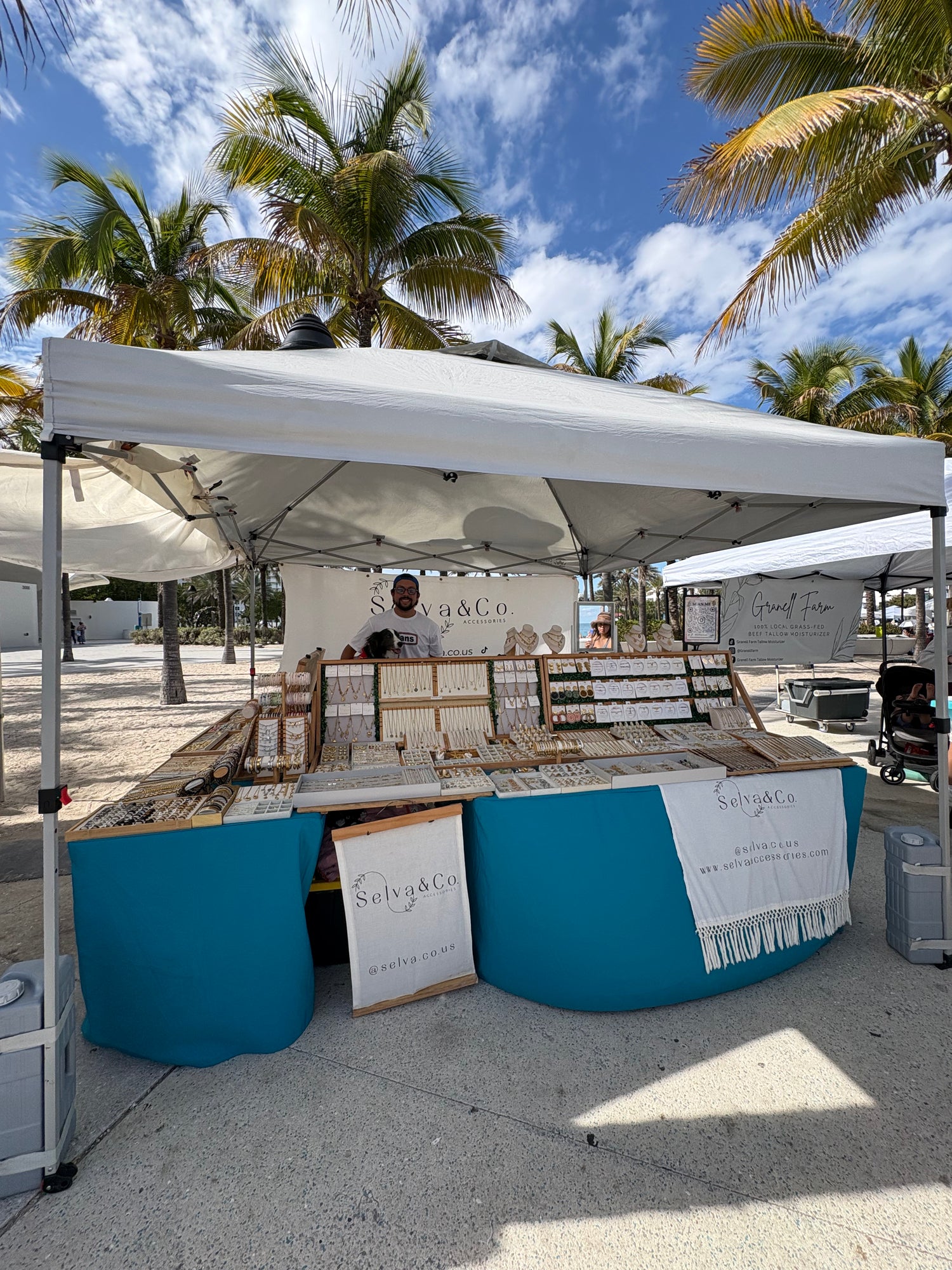 Outdoor market stall with blue and white decor under a canopy, surrounded by palm trees.