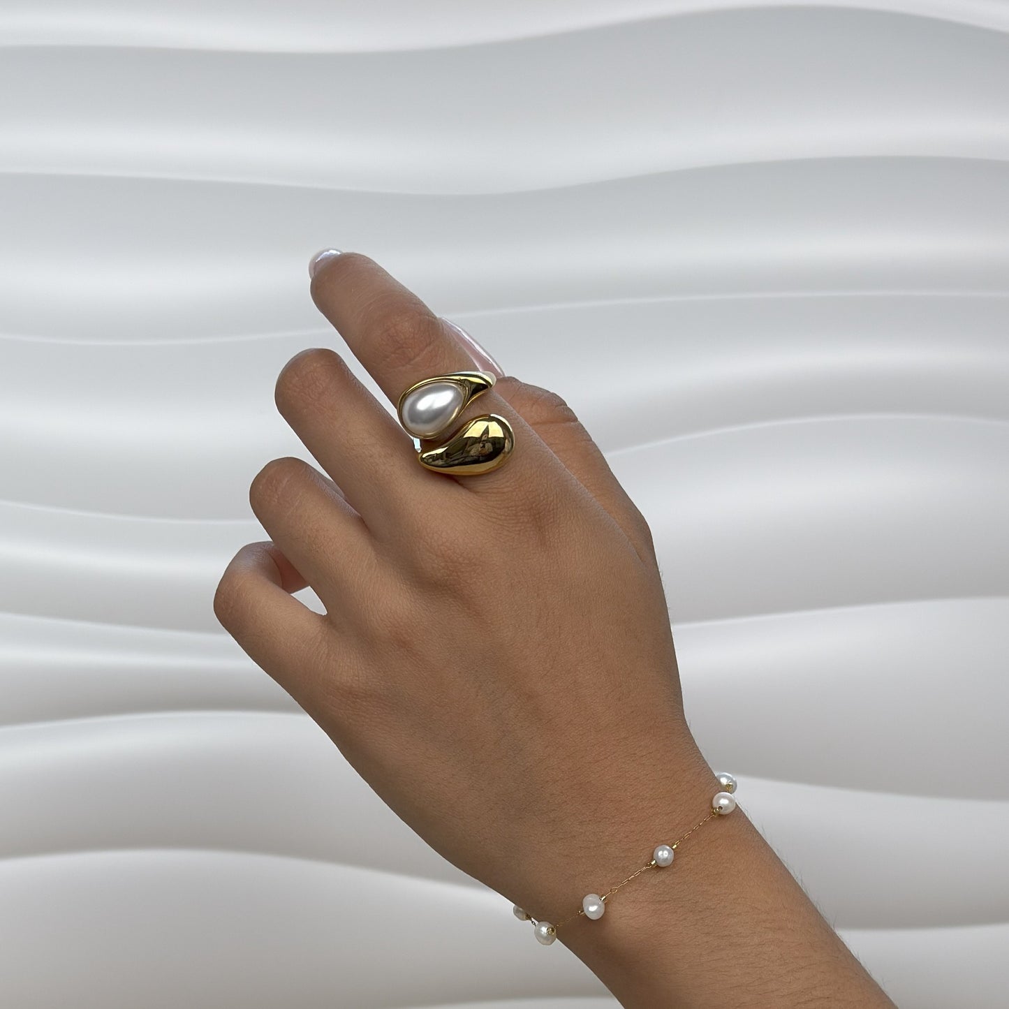 Hand wearing a gold ring with a pearl and a matching pearl bracelet on a white background