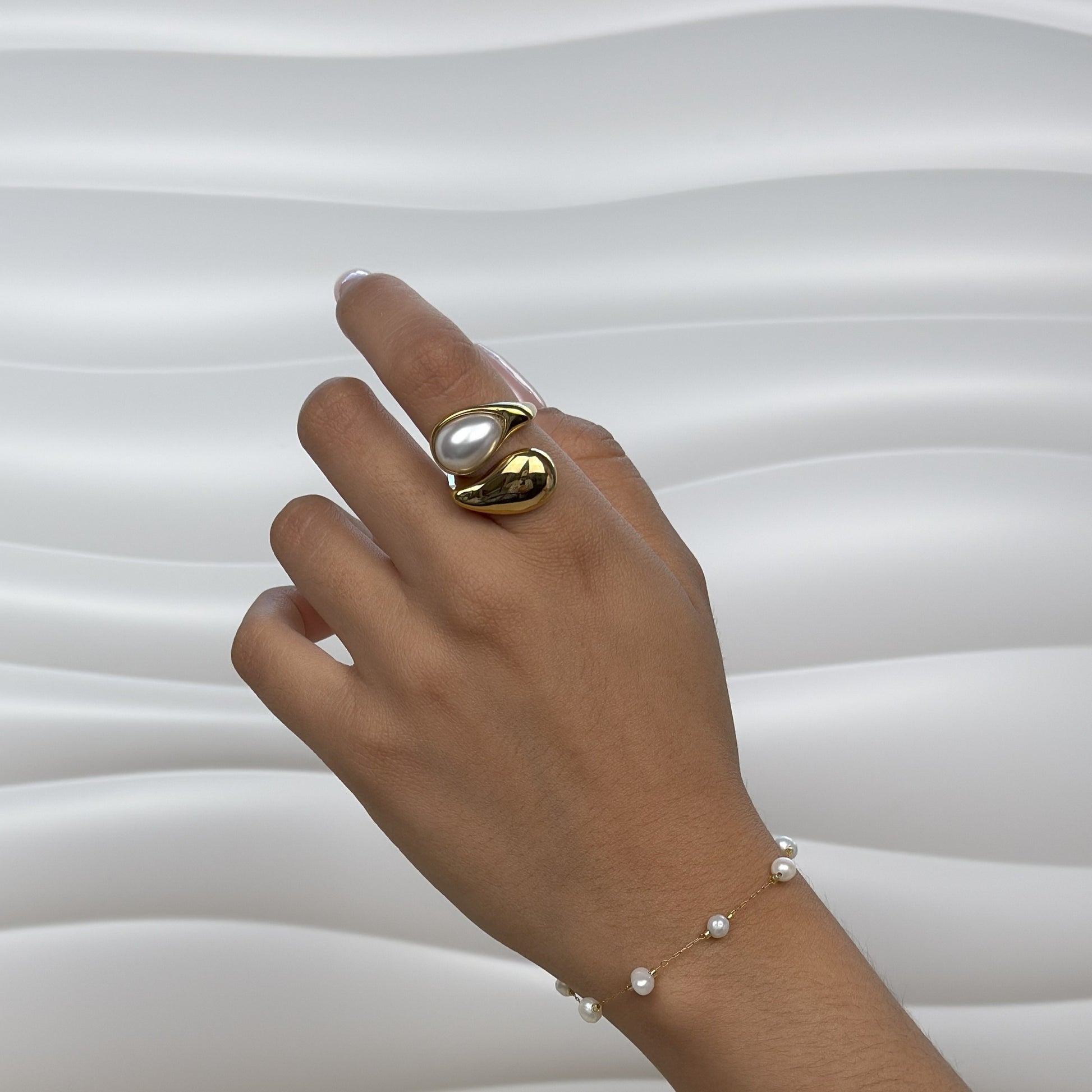 Hand wearing a gold ring with a pearl and a matching pearl bracelet on a white background
