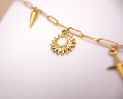 Statement necklace featuring pearl, sun, and spike pendants on a gold chain.